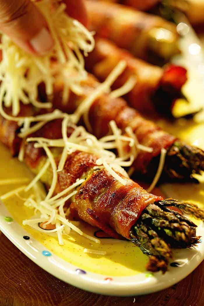 Grilled Bacon Wrapped Asparagus being sprinkled with parmesan cheese.