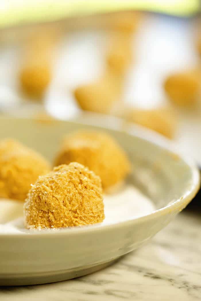 Raw cookie dough balls being rolled in sugar.