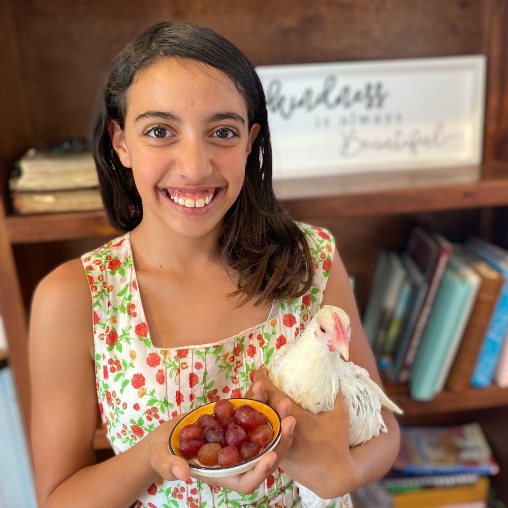 Girl holding a chicken and a small plate of grapes