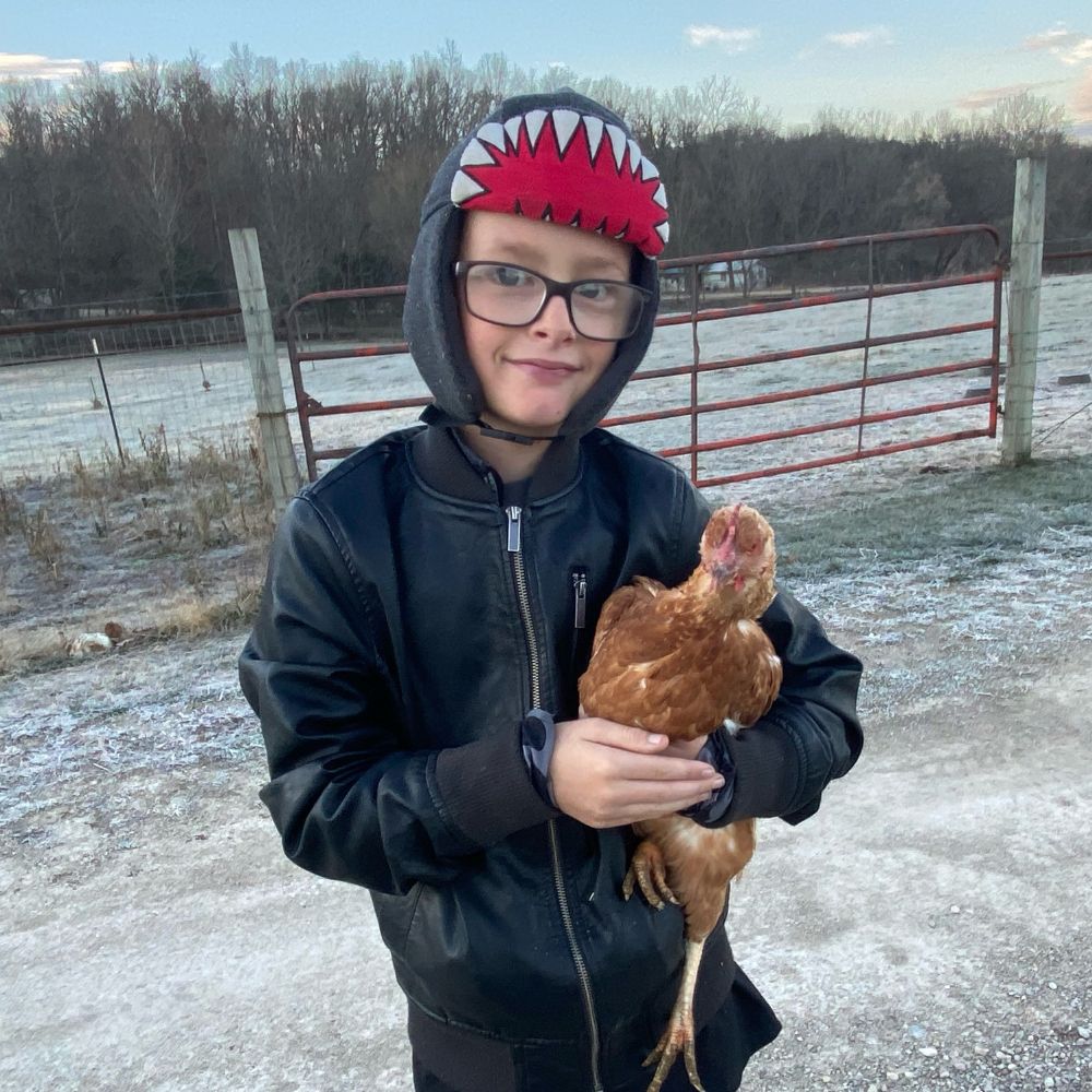Boy holding ISA Brown chicken with frosty cold field in background