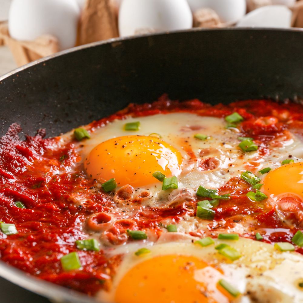 Eggs being cooked in frying pan with tomato sauce and chives