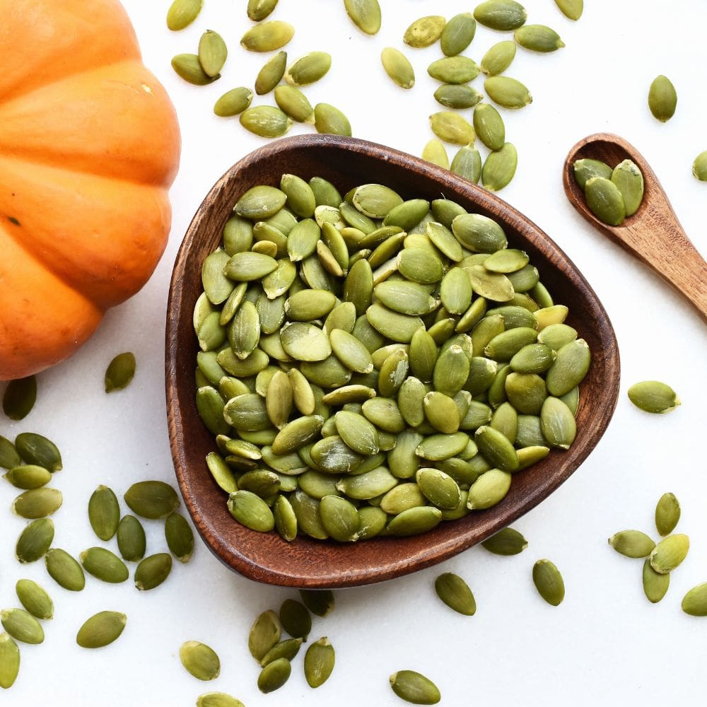 Dish of pumpkin seeds sitting next to a pretty orange pumpkin